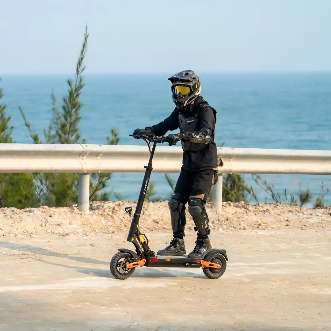 Rider with full helmet and protective gear riding Joyor Y8-S EU legal electric scooter on coastal road with sea background